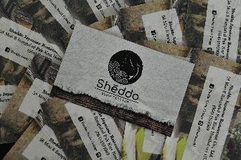 นามบัตร Sheddo ร้านอาหารญี่ปุ่น โดดเด่นด้วยสีดำกลางภาพเป็นวงกลมบนแบ็คกราวด์ขาว มีความคล้ายคลึงกับธงชาติญี่ปุ่น